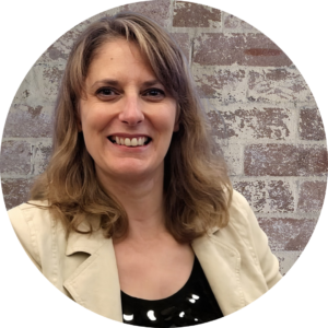 Bookkeeping Services for UK Sole Traders & Small Businesses. Image of Emma (blonde white female) smiling into the camera wearing a black top and cream jack, with a rustic brick wall background.